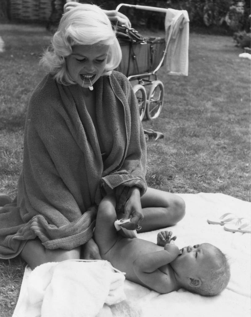 August 1959: Holding a safety pin between her teeth like any other mother, American sex symbol Jayne Mansfield (1933 - 1967) changes the nappy of her son Miklos Hargitay (Mickey Jnr) in the garden. (Photo by Chris Ware/Keystone Features/Getty Images)