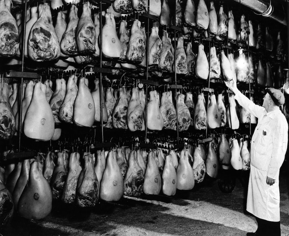 circa 1928: A butcher inspects a rack of hams. (Photo by Three Lions/Getty Images)