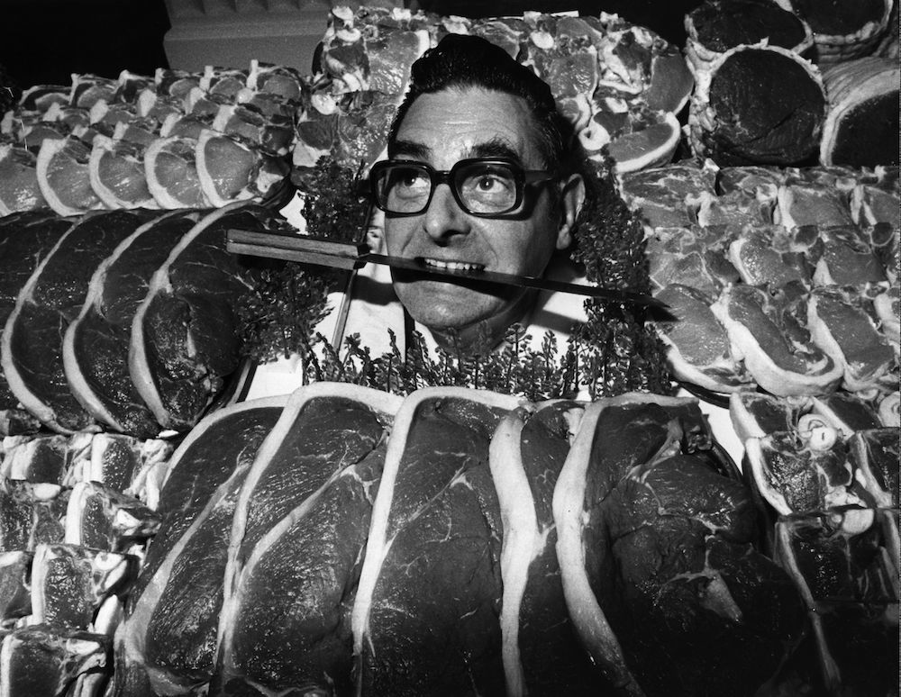 circa 1975: The winner of the Dewhurst's Master Butcher of the Year, James Pegg, poses with a knife between his teeth and a selection of meat. (Photo by Evening Standard/Getty Images)