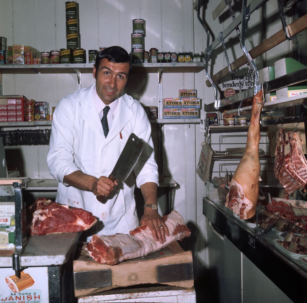 circa 1970: Leyton Orient footballer Peter Brabrook at work chopping meat in his butcher's shop. (Photo by Express/Express/Getty Images)