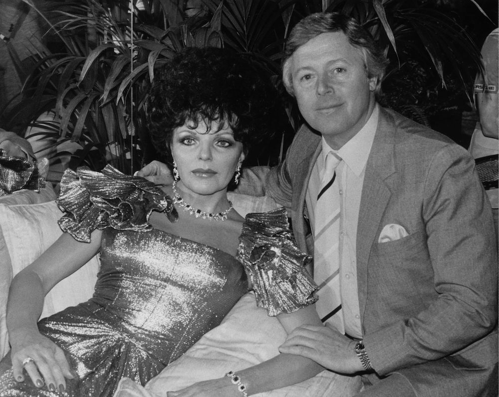 7th January 1986:  Television presenter Michael Aspel sits with a waxwork model of English actress Joan Collins.  (Photo by Keystone/Getty Images)