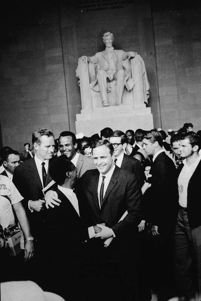 American actor Marlon Brando (1924 - 2004) stands with his arm around poet James Baldwin, surrounded by actors Charlton Heston (L), Harry Belafonte and others gathered at the Lincoln Memorial during the Civil Rights March on Washington, D.C., August 28, 1963. (Photo by Hulton Archive/Getty Images)