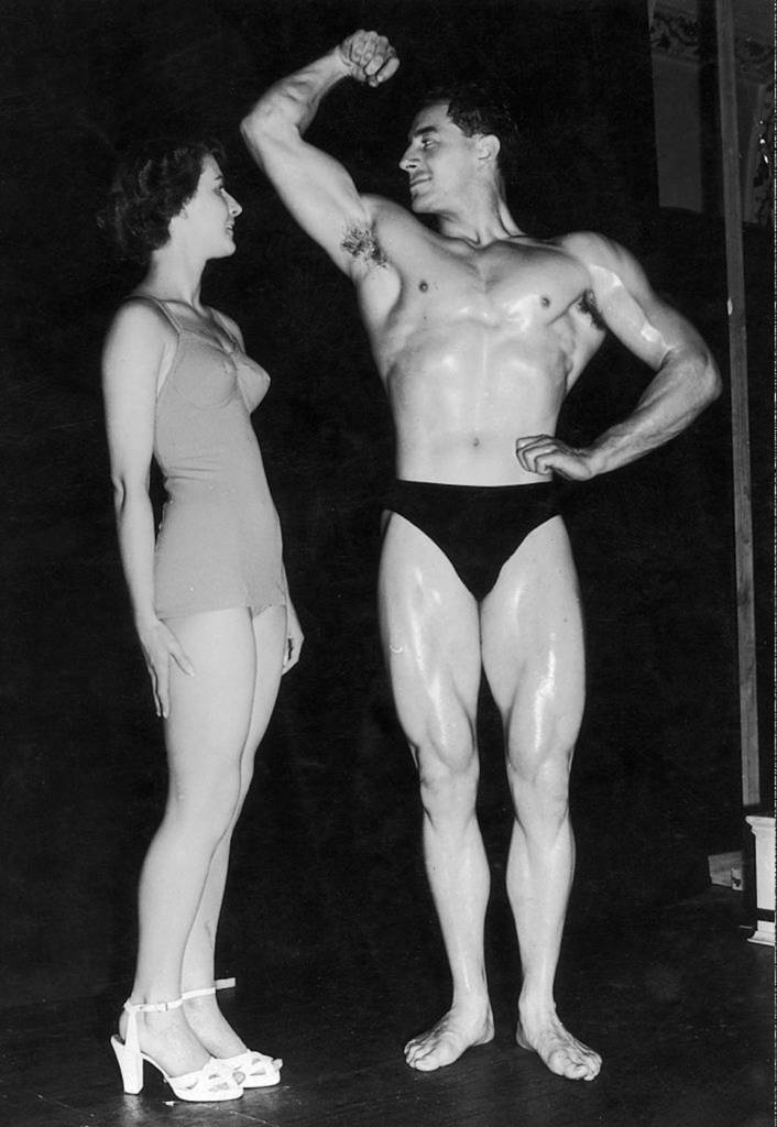 1st September 1951, Mr Universe contestant Arnold Dyson of Liverpool shows off his pecs and biceps to an admiring Norma Tinkler, an entrant in the Junior Miss Britain contest, at the Royal Hotel, London. (Photo by J. Wilds/Keystone/Getty Images)