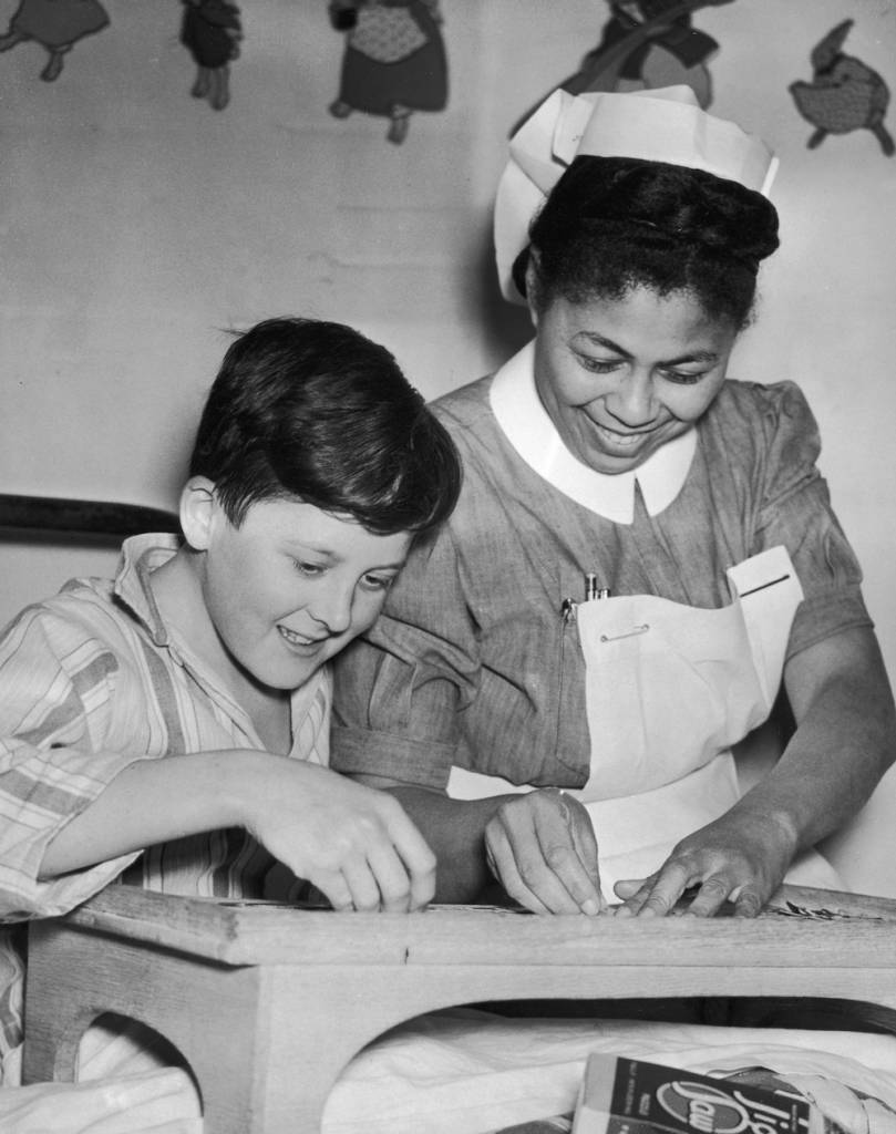 Nurse Hazel Hart from Jamaica helps 13 year-old patient Brian Harris with a jigsaw puzzle at the Princess Alice Hospital, Eastbourne, 7th January 1952. (Photo by George W. Hales/Fox Photos/Hulton Archive/Getty Images)