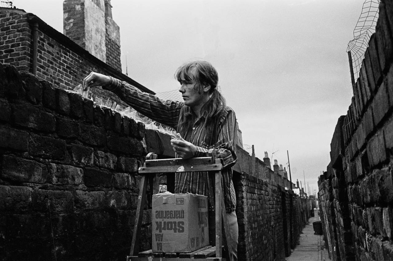 Woman sticking anti burglar glass onto back wall of house Liverpool 8 1971