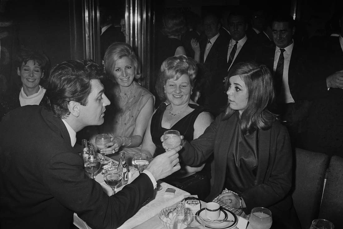 British actor Edmund Purdom (1924 - 2009, left) with Frances Shea (1943 - 1967, right), wife of English gangster Reggie Kray, at the El Morocco, a nightclub owned by the Kray Twins, in Soho, London, 30th April 1965. The Kray twins' mother, Violet Kray, is at centre (in dark dress), sitting to her right is Dolly Kray, wife of Charlie. Actress Adrienne Corri is at far left. (Photo by Larry Ellis/Daily Express/Hulton Archive/Getty Images)