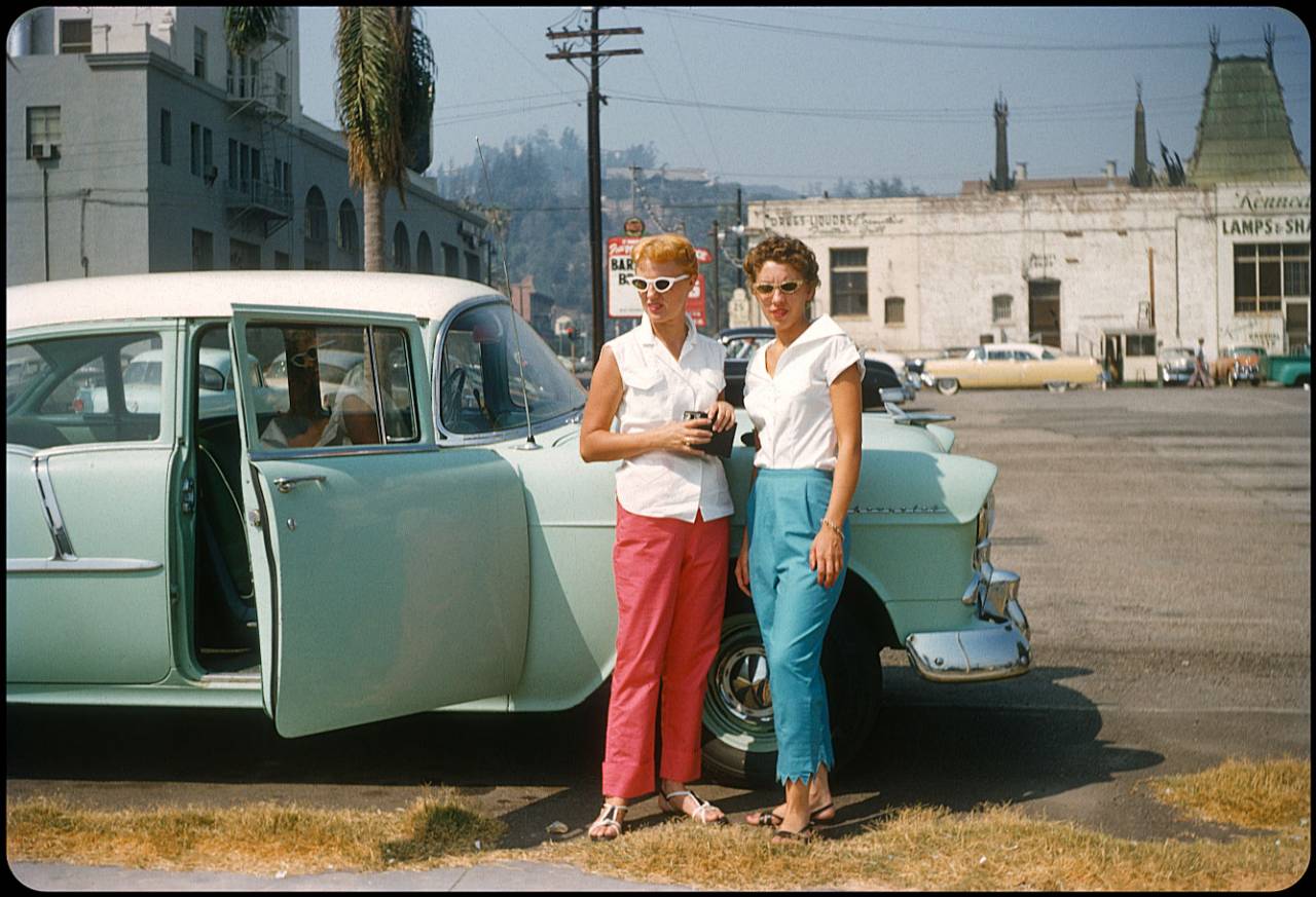 Hollywood! 1956 A couple of hip chicks from Illinois strike a pose behind the Hollywood Roosevelt Hotel and Grauman's Theater on N. Orange. The mint green 1955 Chevy 210 4-door sedan sets off the girls' red and blue slacks, and you almost miss the zig-zag alteration on miss blue-pants. She looks like trouble...