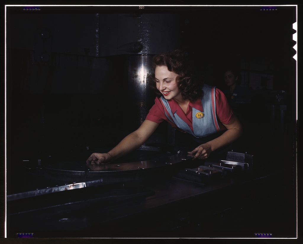 Metal parts are placed on masonite by this woman employee before they slide under the multi-ton hydropress, North American Aviation, Inc., Inglewood, Calif.