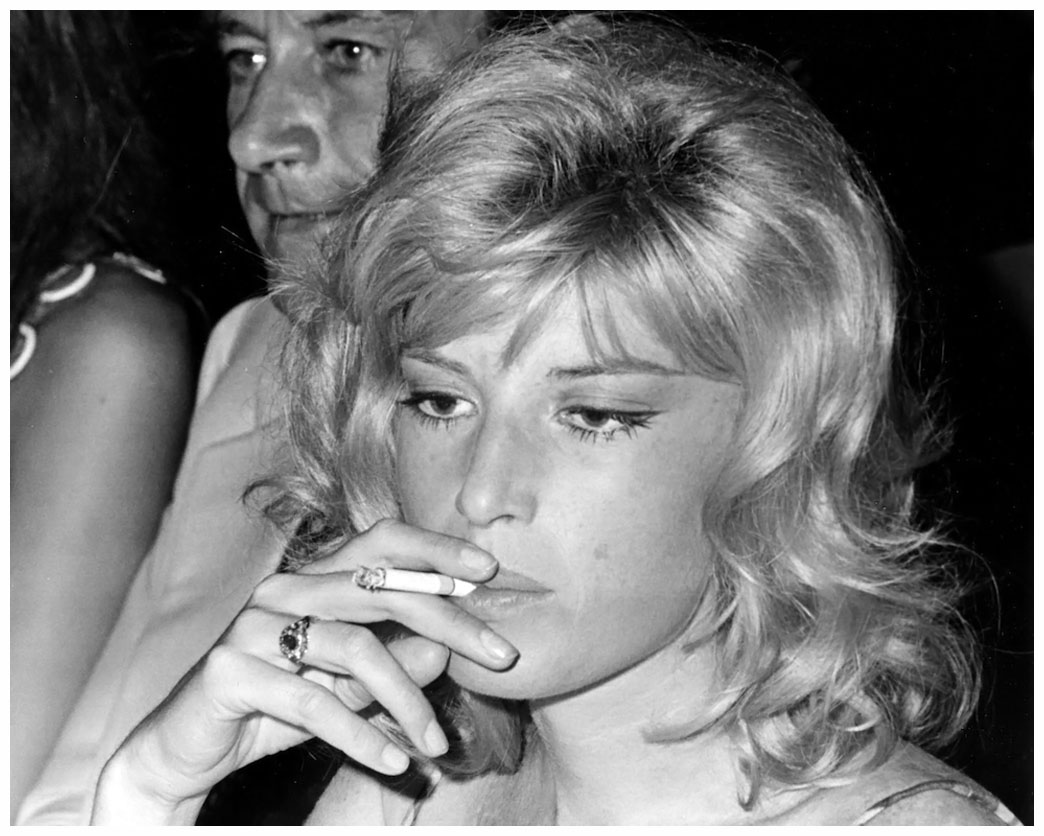 Portrait of Italian actress Monica Vitti smoking a cigarette and producer director Gualtiero Jacopetti (partially obscured behind Vitti) attend a party for movie celebrities in a fashionable night club in Rome, Italy, July 6, 1968. (AP Photo/Gianni Foggia)