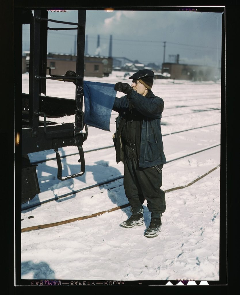 John Paulinski, car inspector, blue flagging a train for inspection, at Corwith yard, Santa Fe RR trip, Chicago, Ill. 1 transparency : color. Contributor: Delano, Jack Date: 1939