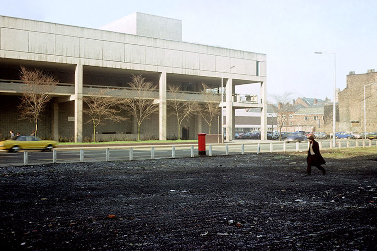 View across Oxford Road to the Royal Northern College of Music in 1976. Shows the high-level pedestrian walkway that was intended to link the RNCM to other buildings in the 'Manchester Educational Precinct'. The RNCM was designed by Bickerdike, Allen, Rich & Partners and built 1968-73. The University of Manchester's Business School (East) building now occupies the open space in the foreground.