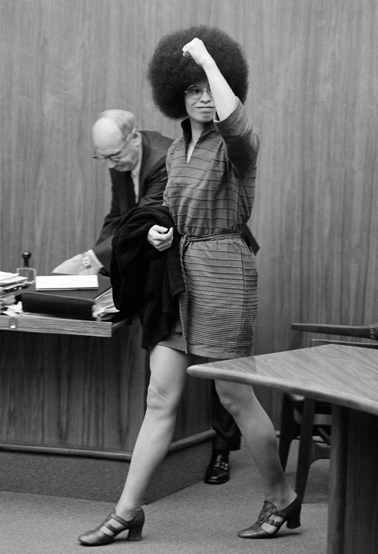 Angela Davis waves to someone in the audience as she arrives the room in San Rafael, Calif. for another pre-trial hearing. At left is chief attorney, Howard Moore Jr of Atlanta. holding the door Miss Davis is Capt. Harvey Teague of the Marin County Sherriffs Department Angela Davis, San Rafael, USA