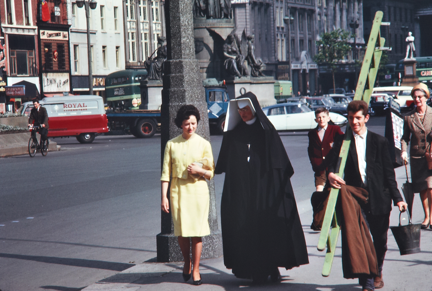 Ireland 1960s, Photographer Richard Tilbrook captured a fine array of pedestrians in this shot - "ordinary" women; a nun; a schoolboy; a window cleaner; and a cyclist. Also in evidence is the haphazard parking down the middle of O'Connell Street that would give a modern traffic warden pause for thought. Signage for the Confectioner's Hall (second frontage from the left) is still there today, and think that may be Cafolla's Italian Chippers next door... Date: June 1963