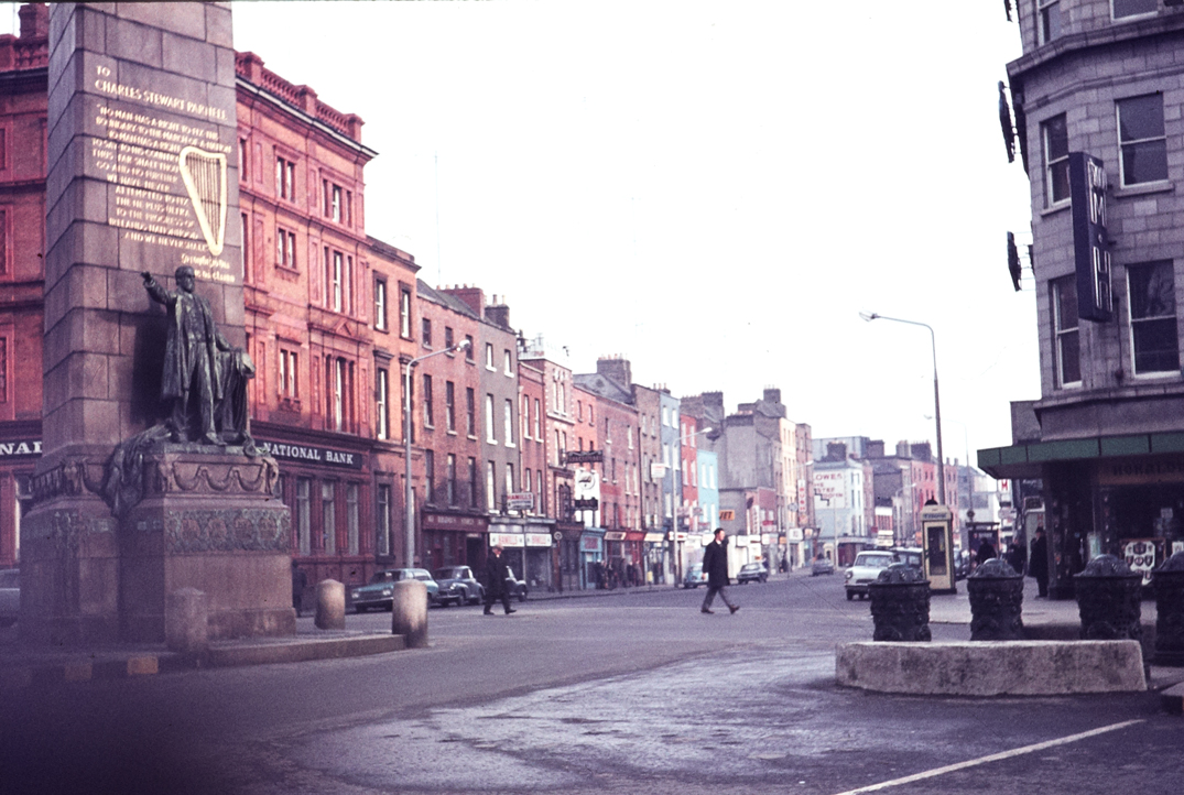 Ireland 1960s, Good shot of the Parnell Monument at the junction of Upper O'Connell Street, Parnell Street and Cavendish Row, Dublin. The ornate bollards are no longer to be seen. Does anyone know what they were? And note the lovely old creamy-coloured telephone box. The text on the Monument is from a passionate speech in support of Home Rule for Ireland that Charles Stewart Parnell gave in Cork on 21 January 1885: "... No man has the right to fix the boundary of a nation. No man has the right to say to his country, "Thus far shalt thou go and no further", and we have never attempted to fix the "ne plus ultra" to the progress of Ireland’s nationhood, and we never shall." Date: Circa 1969