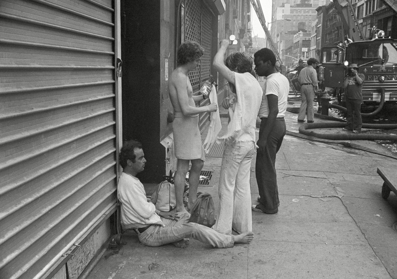 Several guests of the Everard Baths in mid-Manhattan in New York finish dressing on the sidewalk as fire routed the occupants of the building, . Nine persons died in the blaze and more than a dozen were injured. The search for victims will continue 25 May 1977