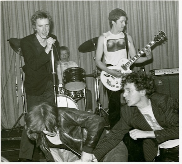 sex pistols Johnny Rotten, Paul Cook and Steve Jones play on as their manager Malcolm McLaren fights with an audience member, April 23, 1976. Photo: Kate Simon