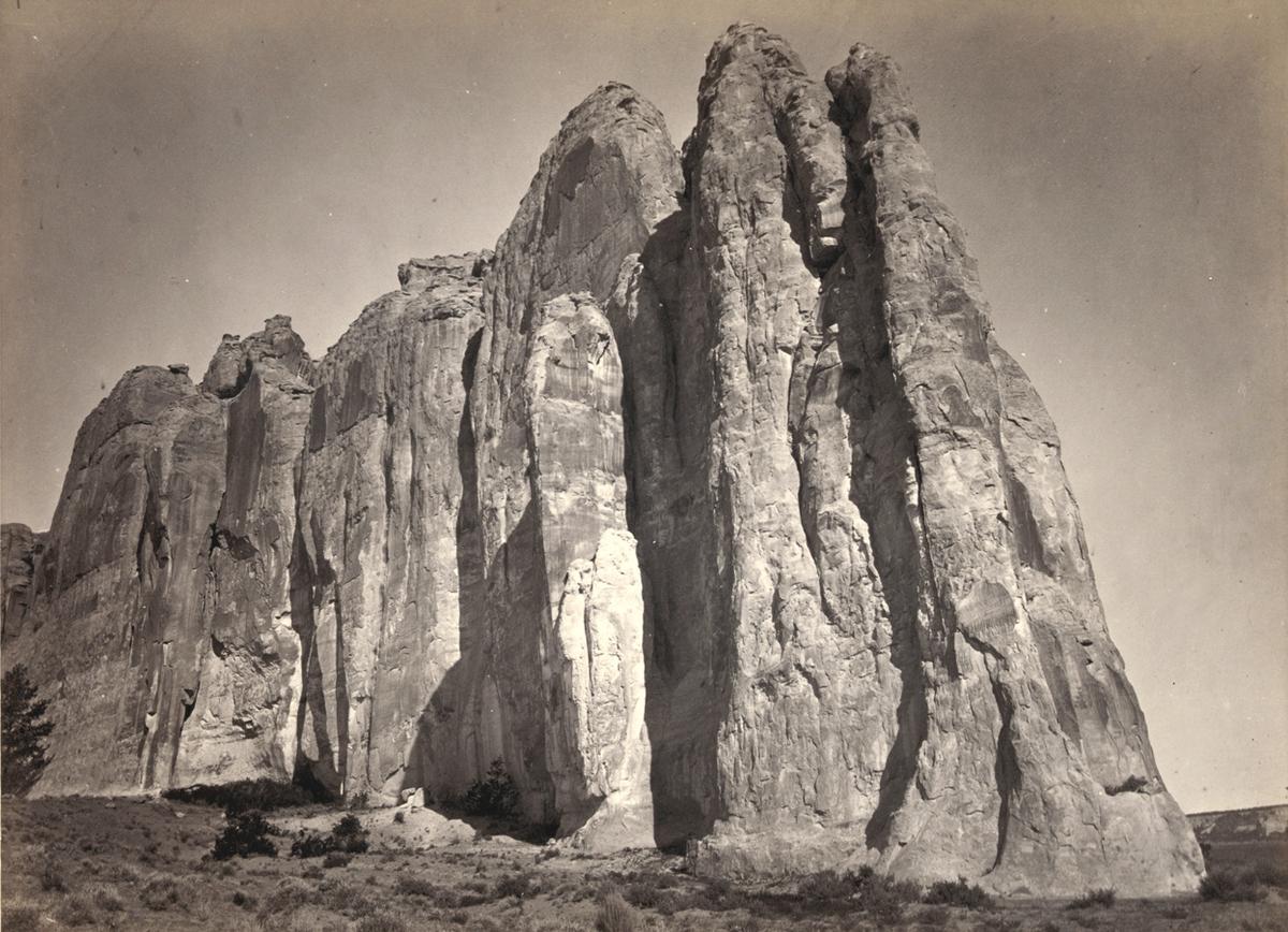 The south side of Inscription Rock (renamed El Morro National Monument), in New Mexico - 1873. Note the small figure of a man standing at bottom center. The prominent feature stands near a small pool of water, and has been a resting place for travelers for centuries. Since at least the 17th century, natives, Europeans, and later American pioneers carved names and messages into the rock face as they paused. In 1906, a law was passed, prohibiting further carving
