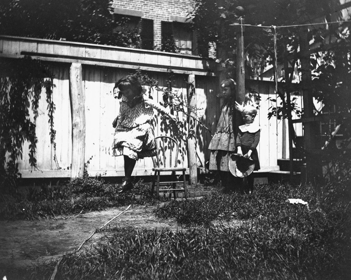 June 20, 1886 Mildred Grimwood jumps in the backyard at 314 Livingston Street as brother Victor Grimwood and pal Zelma Levison look on.