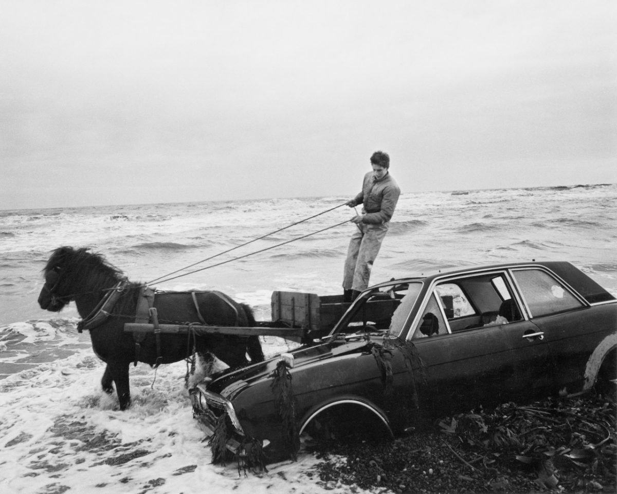 A Car Dumped on the Beach Has to Be Outmanoeuvred by the Seacoalers, Lynemouth, Northumberland, UK, 1982 © Chris Killip