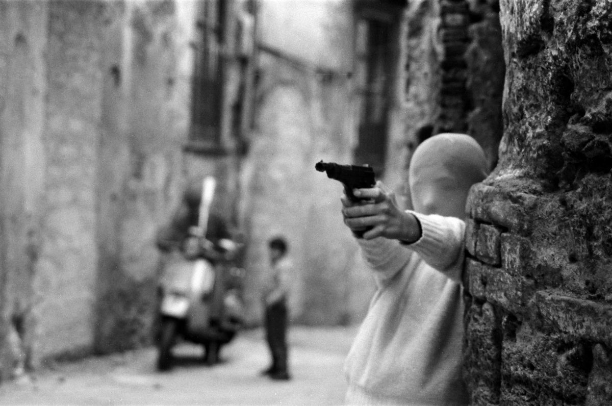 A boy in a stocking mask points a pistol mafia Sicily Italy 