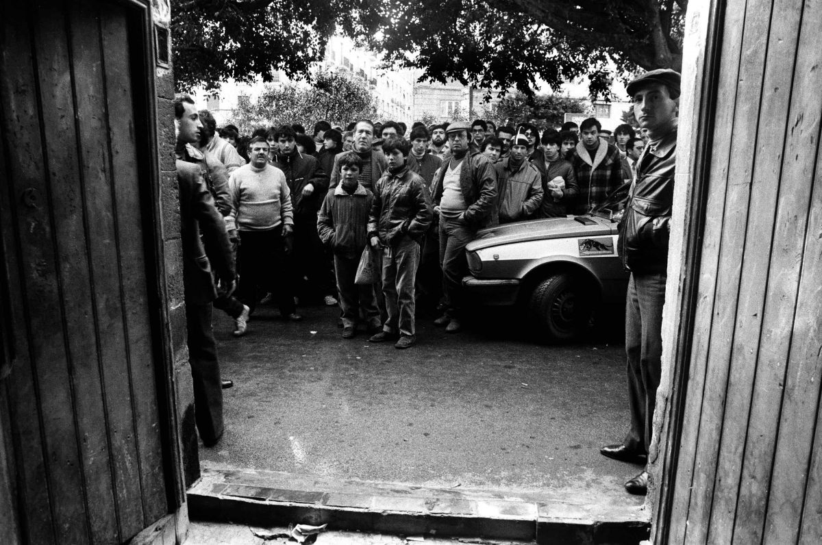 A crowd of onlookers stands in front of a doorway mafia Sicily Italy 