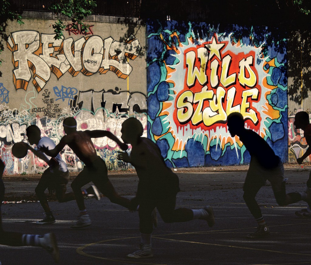 Men running on basketball court in front of colorful graffiti