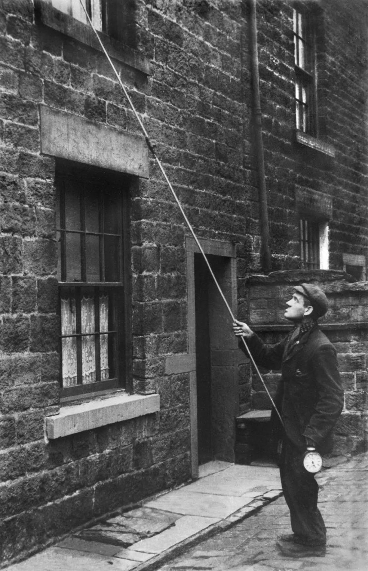 Young man taps on a second-floor window with a long pole