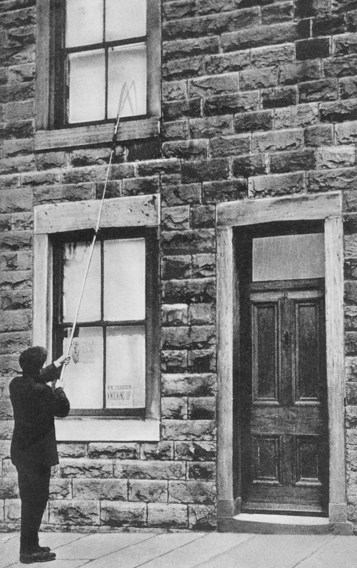 A man taps on a second-floor window with a long pole