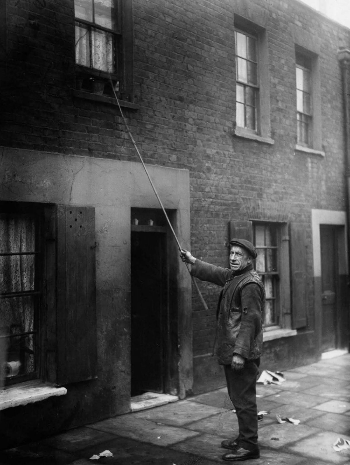 Older man taps on a second-floor window with a long pole