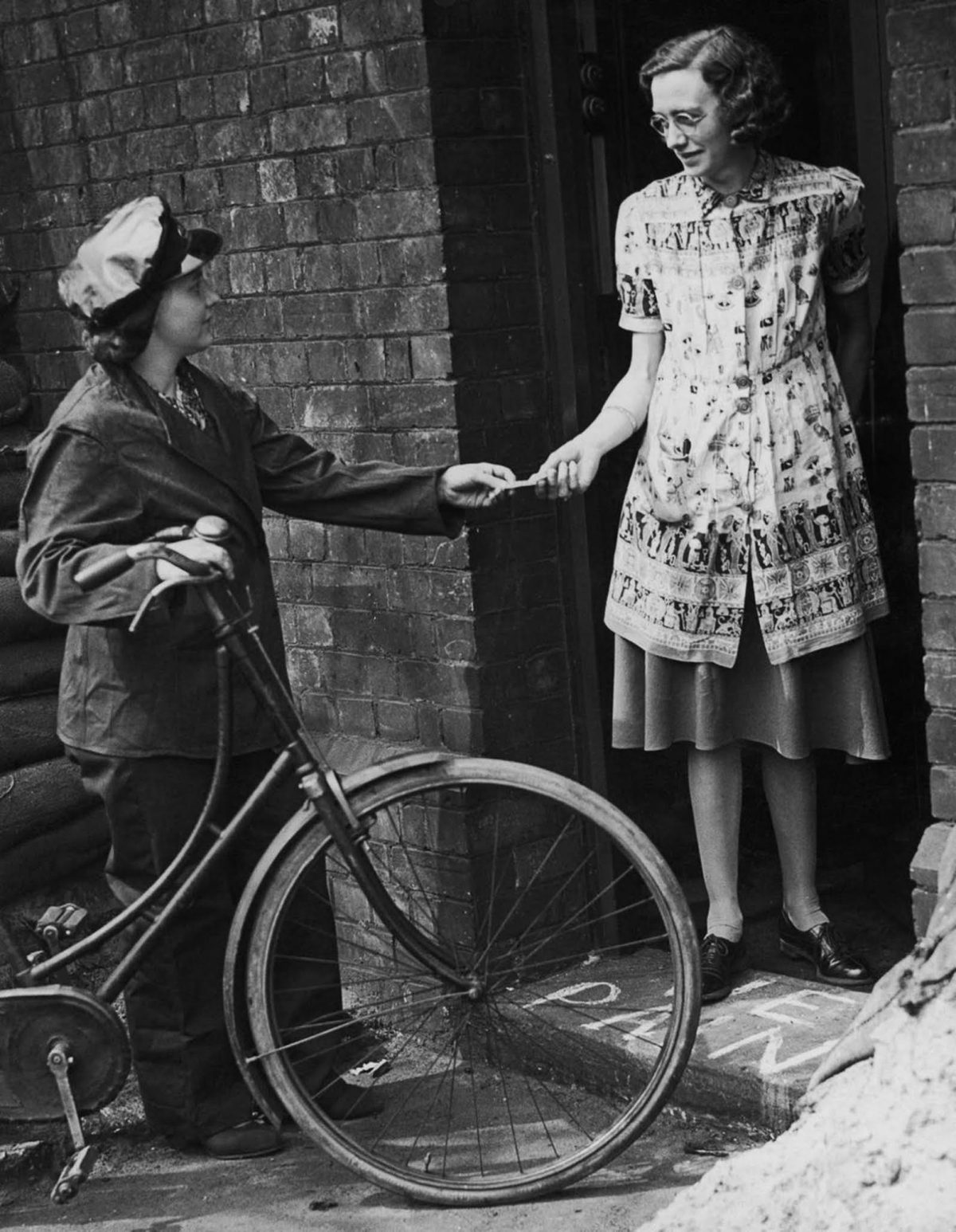 A woman on a bicycle hands another woman a message