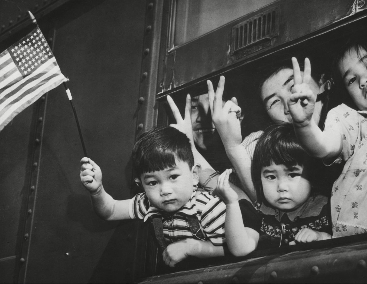 Japanese-American children waving from a train window as it leaves Seattle to take them to an internment camp for the duration of World War II. March 1942.