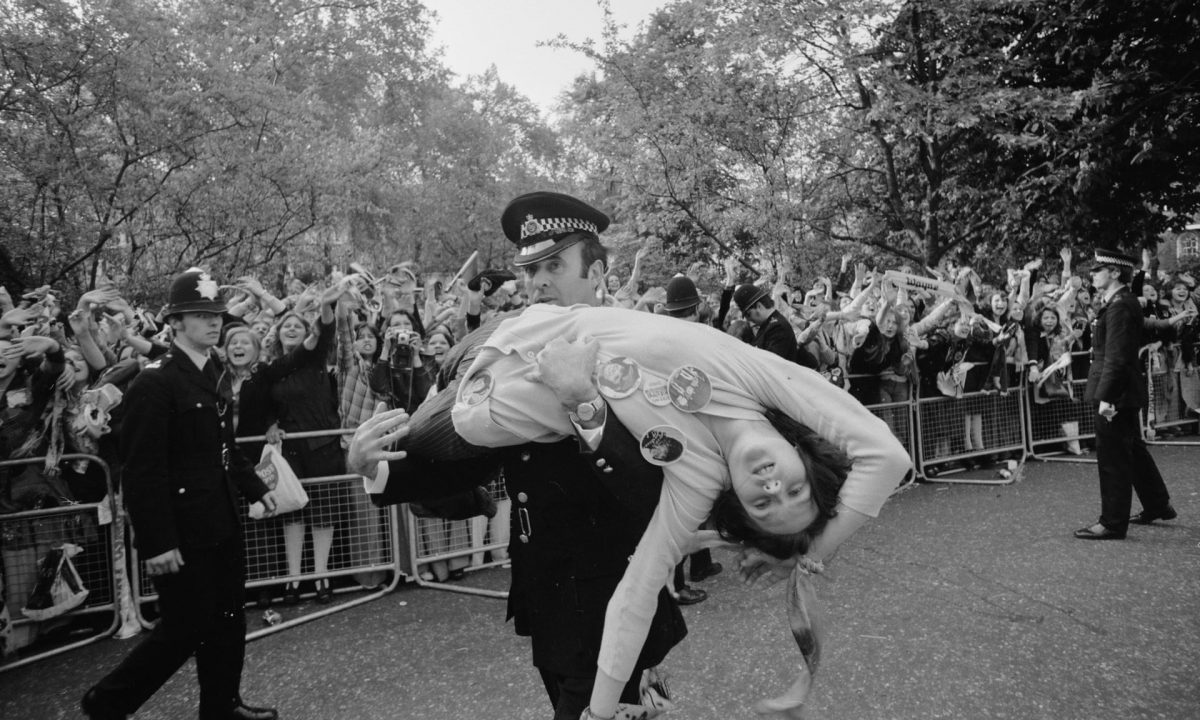 A policeman carries away a fan injured in the crush to see members of The Osmonds pop group on the balcony of a hotel in Belgravia, London, 27 May 1975