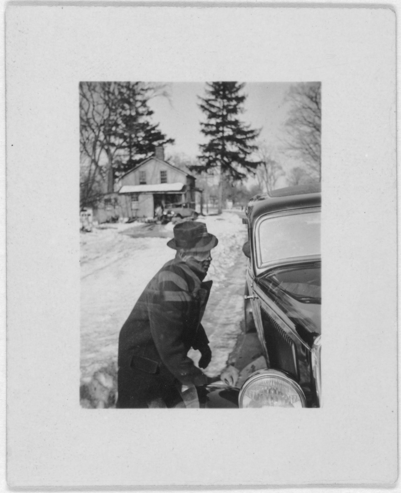 Leadbelly, three-quarter-length, profile, facing right, lifting car out of snow, at the home of Mary Elizabeth Barnicle, Wilton, Conn