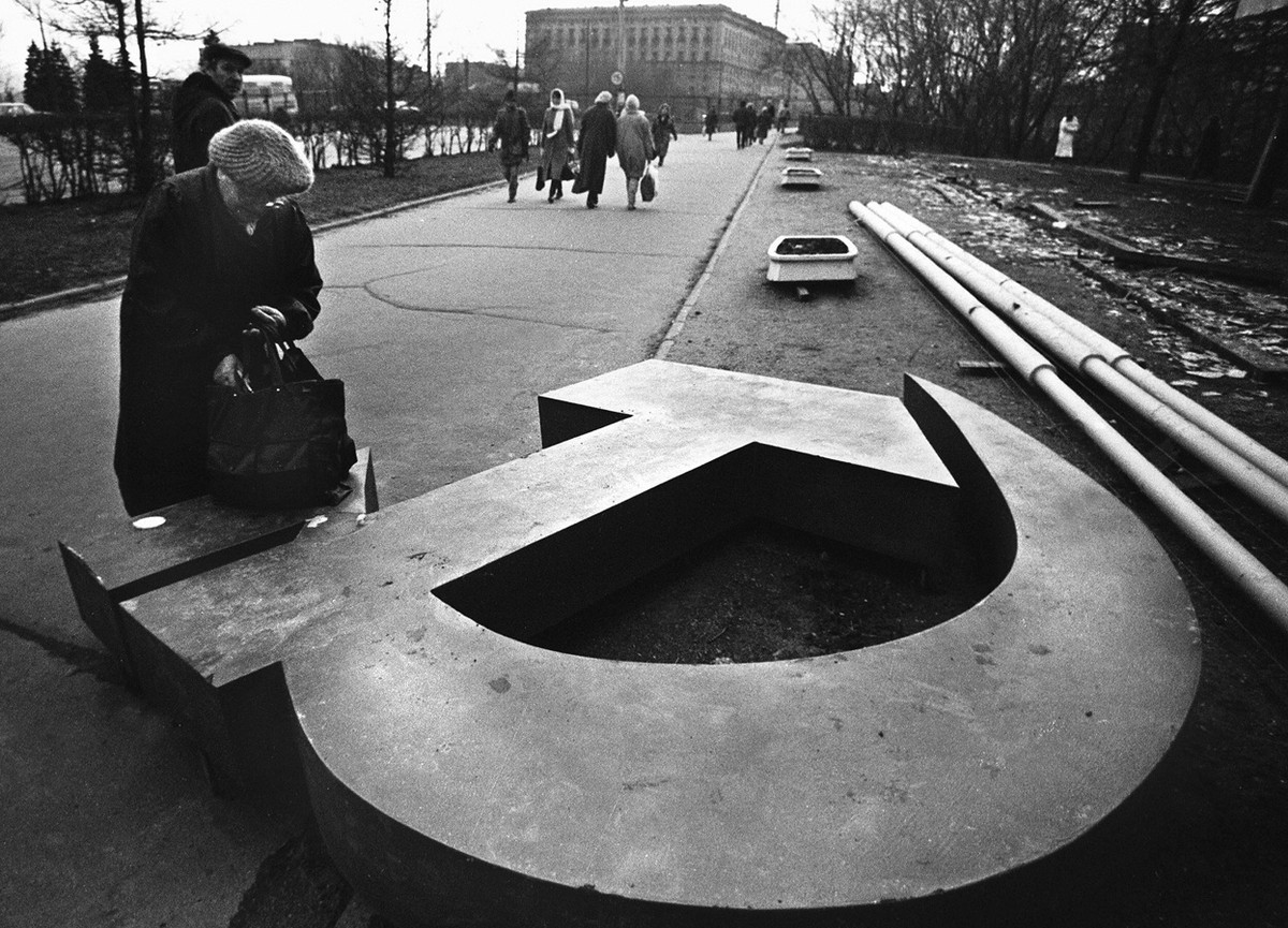 A woman reaches into her bag, which rests on a fallen Soviet hammer-and-sickle on a Moscow street in 1991