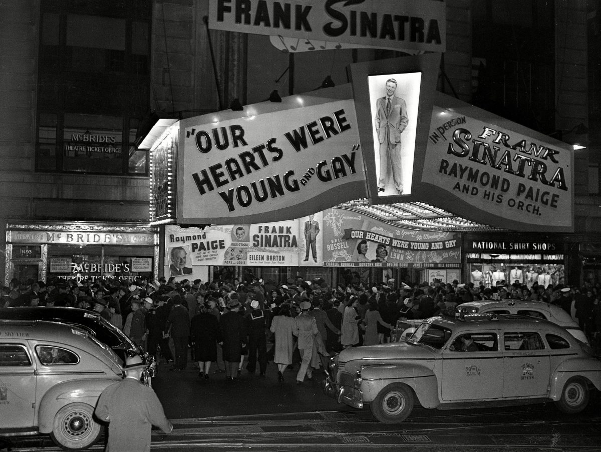 An evening crowd gathers in front of the Paramount Theatre where Frank Sinatra is performing in New York's Times Square, during World War II. Dozens of extra police are on duty to keep the crowd moving 10 Oct 1944