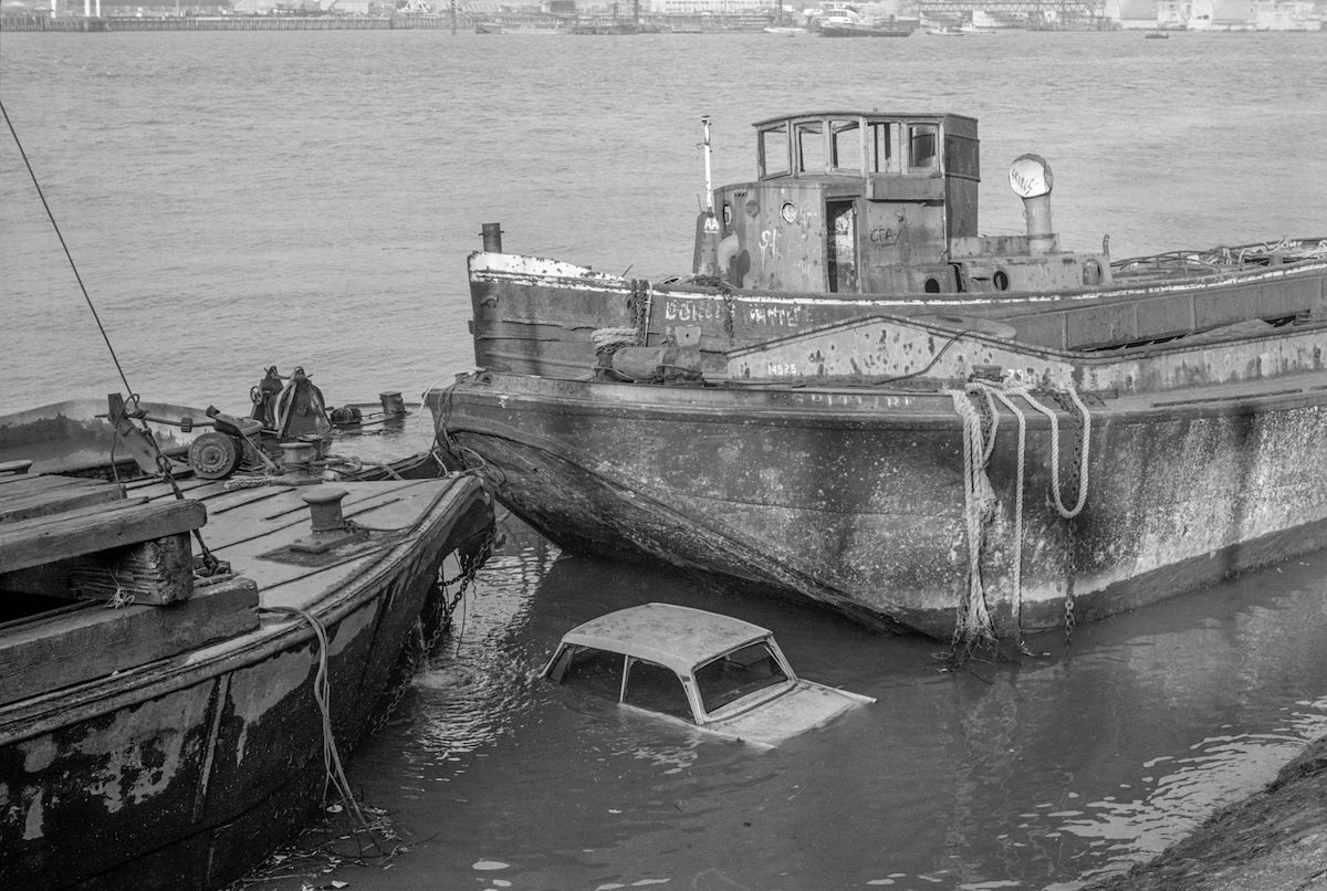 Car and vessels, Riverside, East Greenwich. 1982 30m-23- River Thames, car, lighter, tug