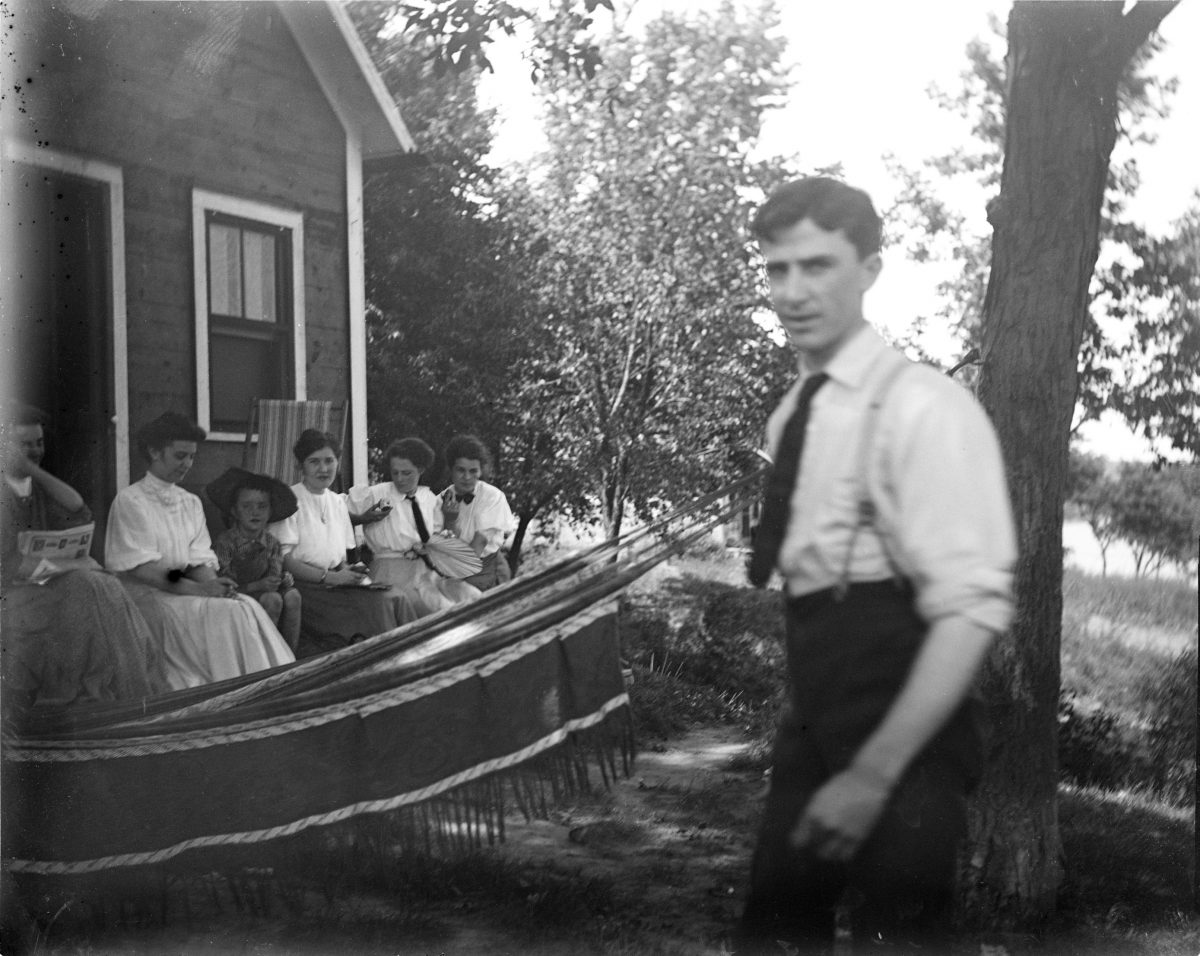 Unidentified man in foreground, five women and boy sitting on porch with hammock in backgroundGeorge Silas Duntley Photographs 1899-1918