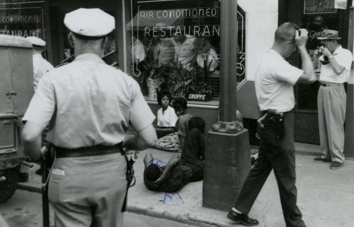On July 26, 1963, student protesters on Main Street in Farmville stage a sit-in outside the College Shoppe restaurant, which refused to serve black patrons. Whites inside the restaurant look out the window as police approach the demonstrators. This protest was part of an organized local campaign against racial discrimination that took place in the summer of 1963.