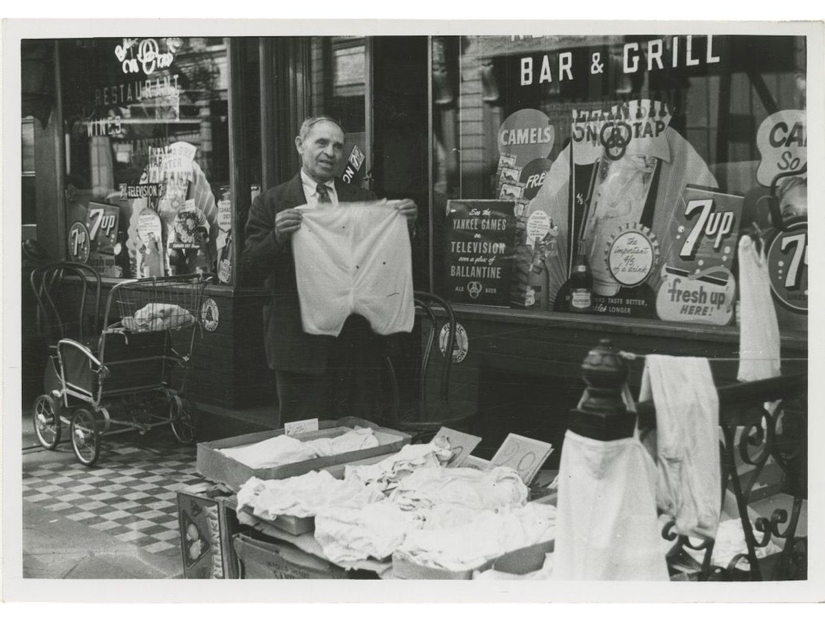 A sidewalk merchant sells clothing in front of a bar and restaurant on the Lower East Side. 1948