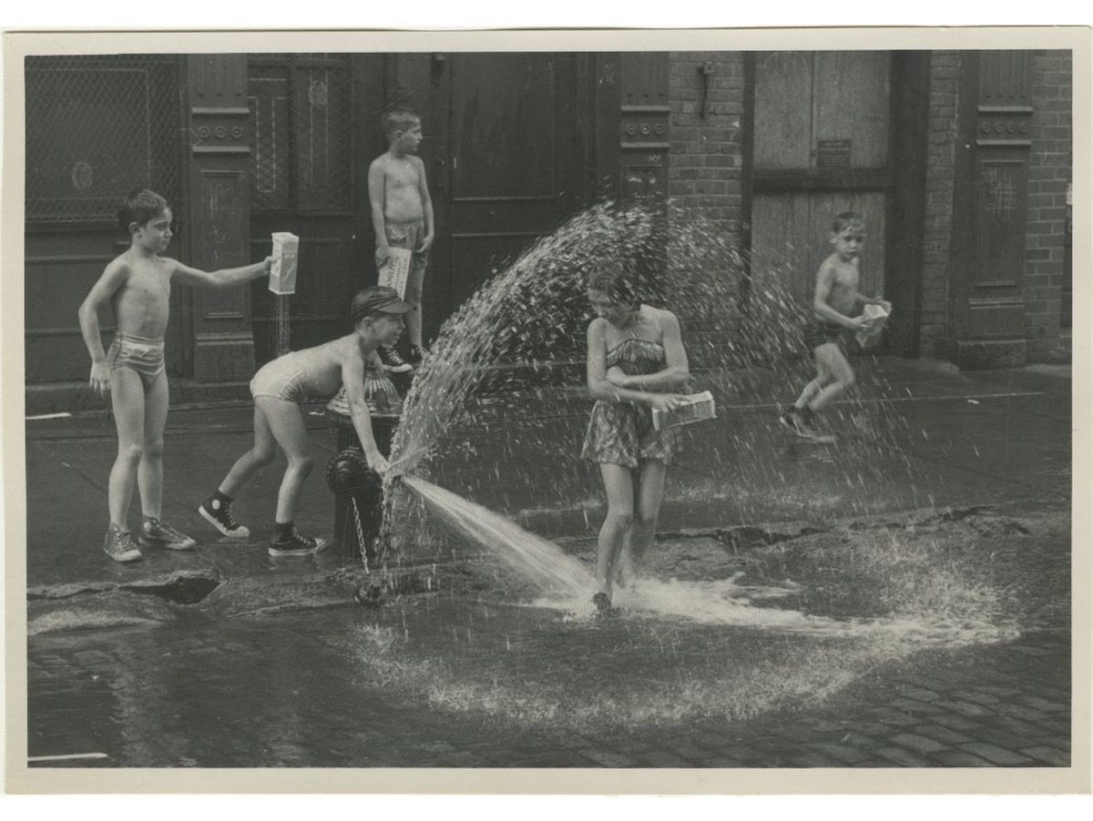 Children play with an open fire hydrant in the street on the Lower East Side
