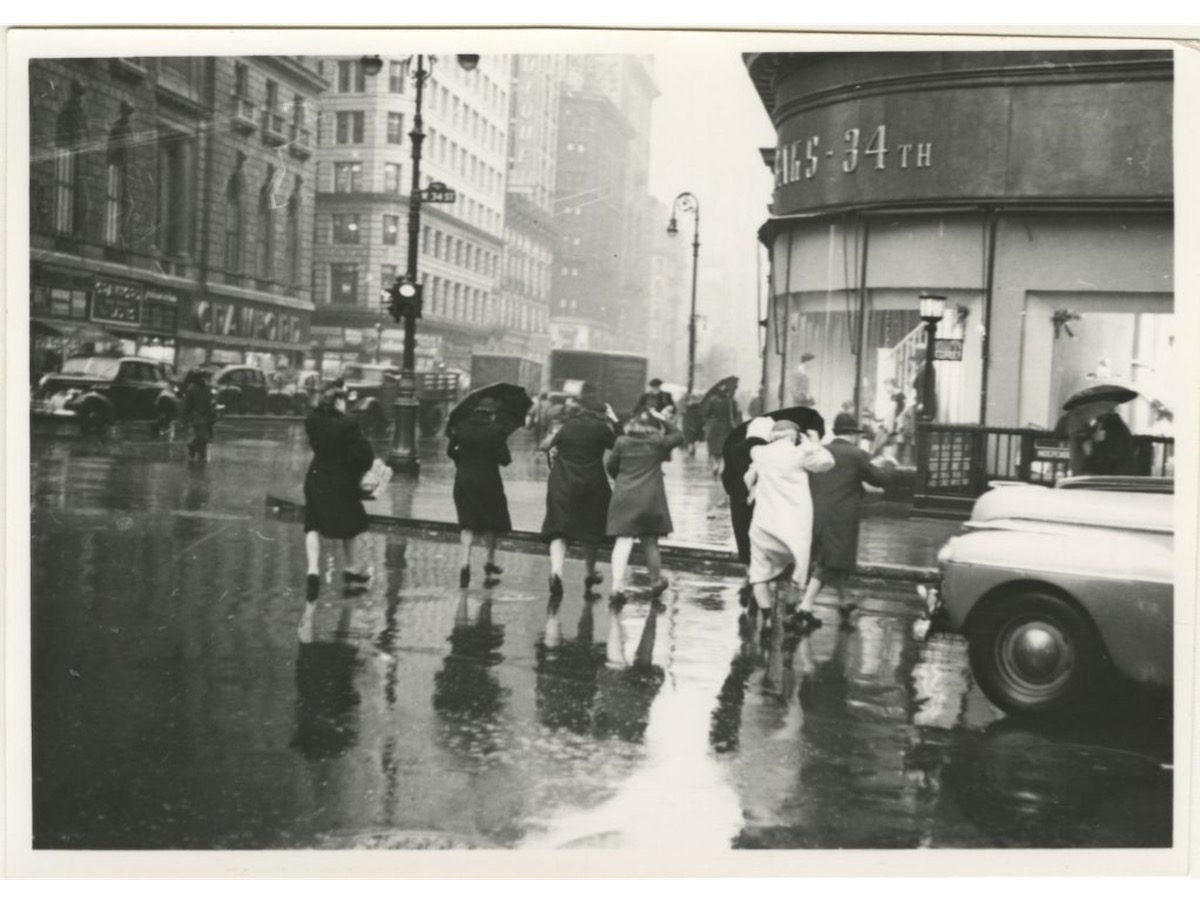Pedestrians cross the street in the rain towards Saks - 34th store on West 34th Street in Midtown Manhattan.