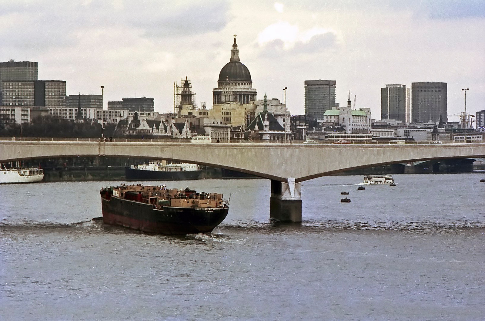 A barge passes beneath Waterloo Bridge with St. Paul's cathedral in the background. 19th April 1975.