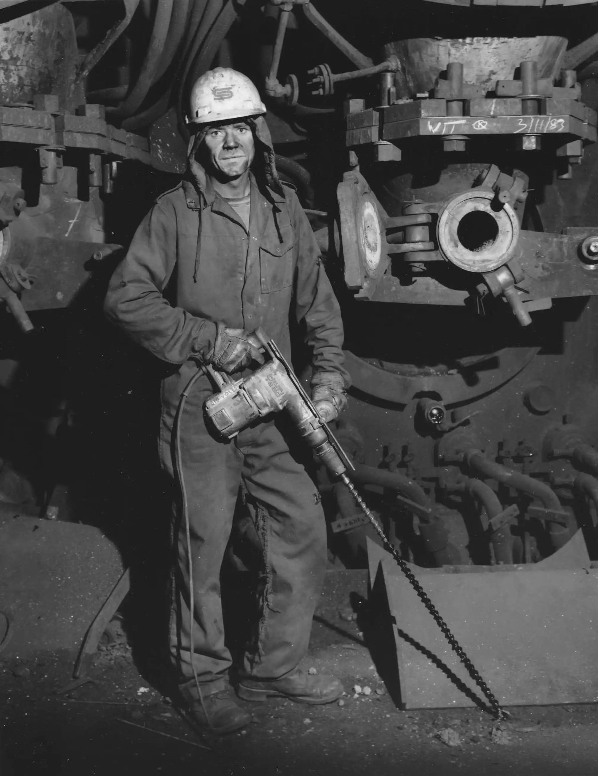 Contract worker drilling out blocked inspection holes below the tuyeres of the Redcar Blast Furnace, Teesside, 1983