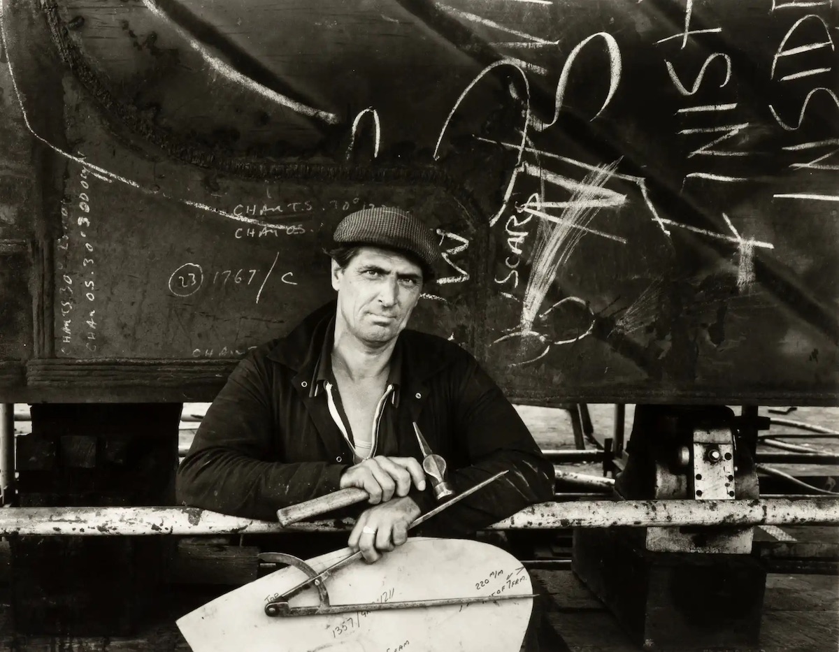 Tony Burke, a shipwright, standing beneath the stern of 1360 Ship, 1986