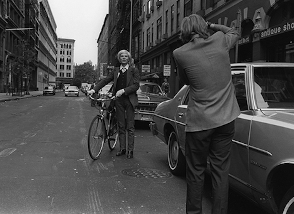 Andy Warhol with a bicycle on East 11th Street in the Village in New York City, Robert Levin, 1981