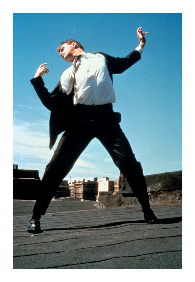 Imagem de uma mulher vestindo roupa formal com o corpo contorcido sobre um terraço em Nova York. Fotografia de Robert Longo