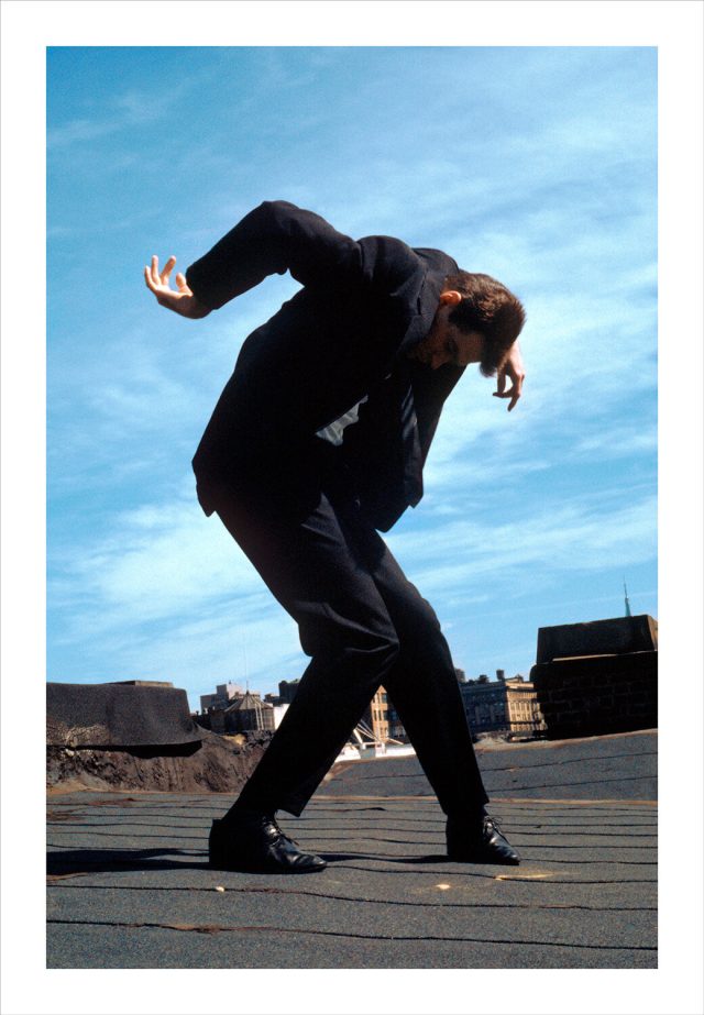Imagem de um homem vestindo terno com o corpo contorcido sobre um terraço em Nova York. Fotografia de Robert Longo