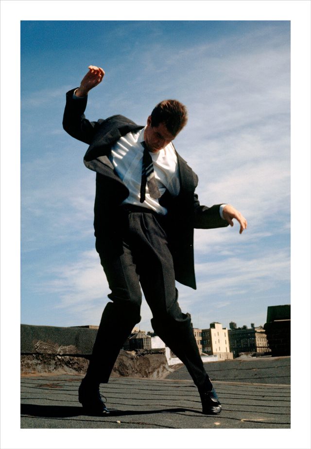 Imagem de um homem vestindo terno com o corpo contorcido sobre um terraço em Nova York. Fotografia de Robert Longo